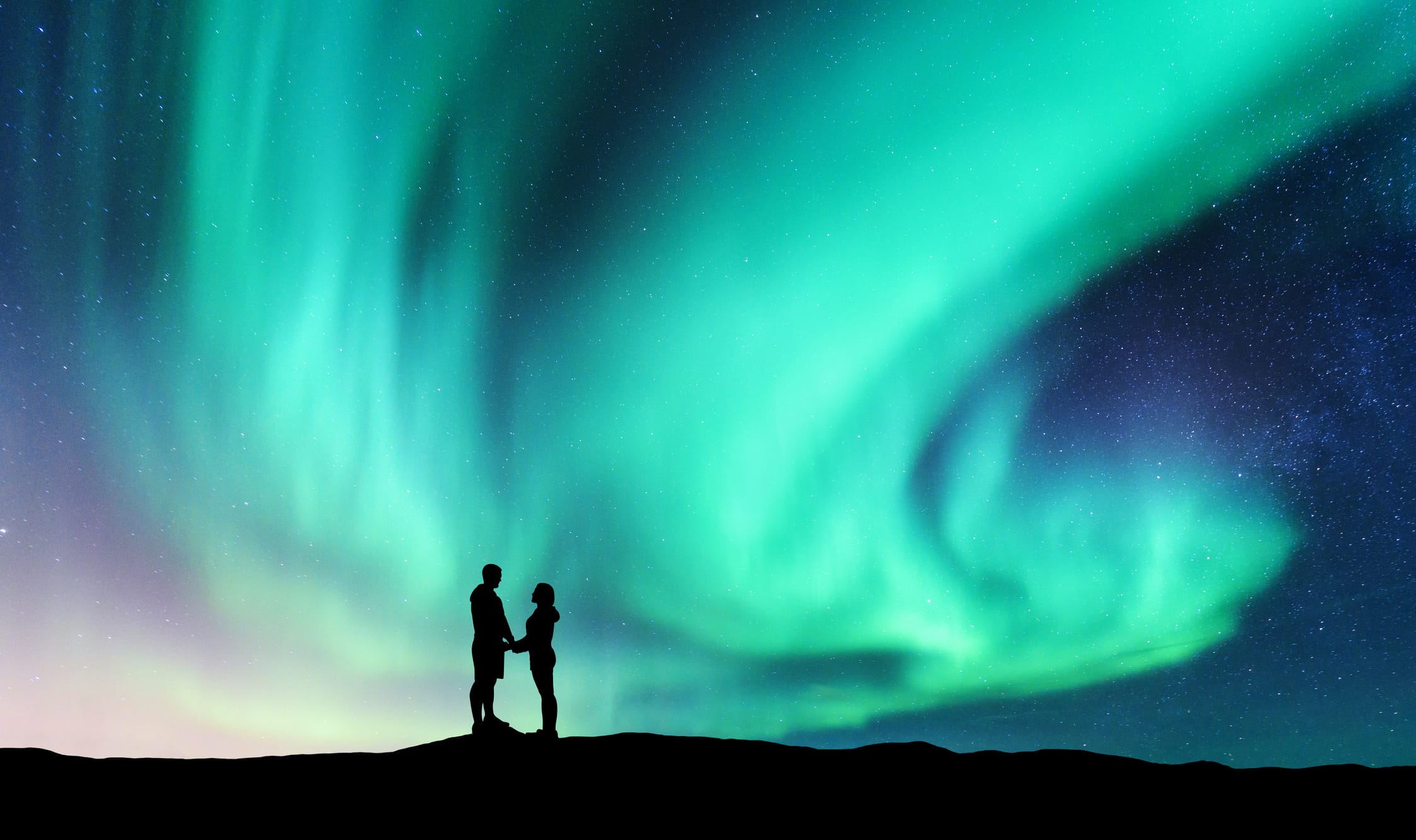 Northern lights and hugging couple on the hill. Landscape with night starry sky, aurora borealis, silhouette of man and woman. People. Concept background with Lovers and polar lights. Nature. Travel