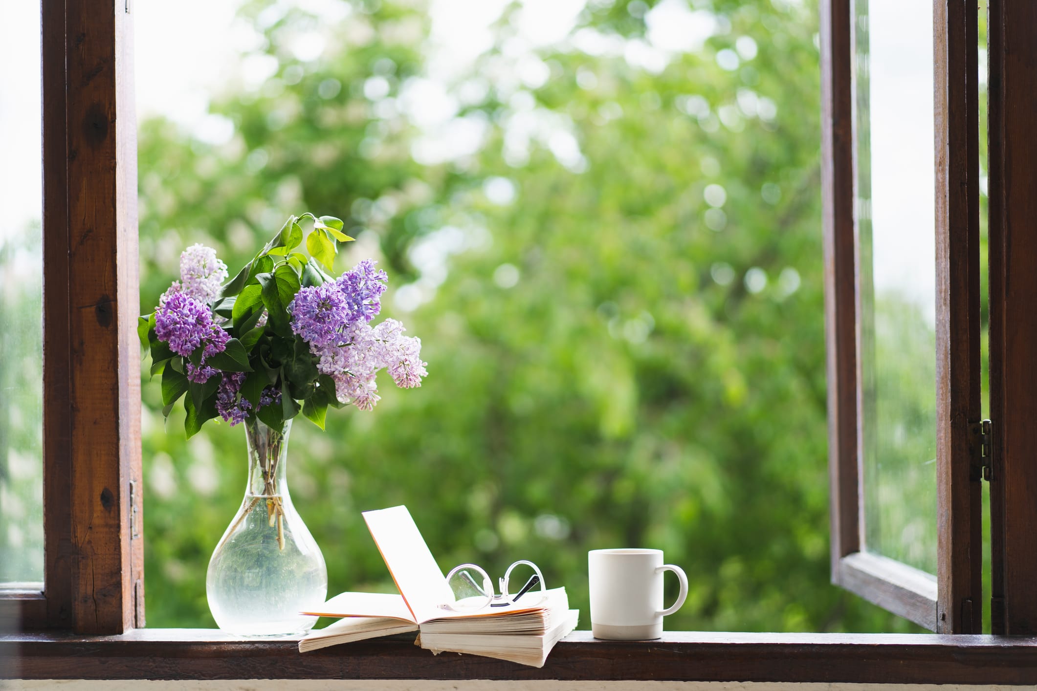 Book, glasses, cup of tea and lilac on a wooden window. Fragrant tea in the garden. Romantic concept. Vintage style