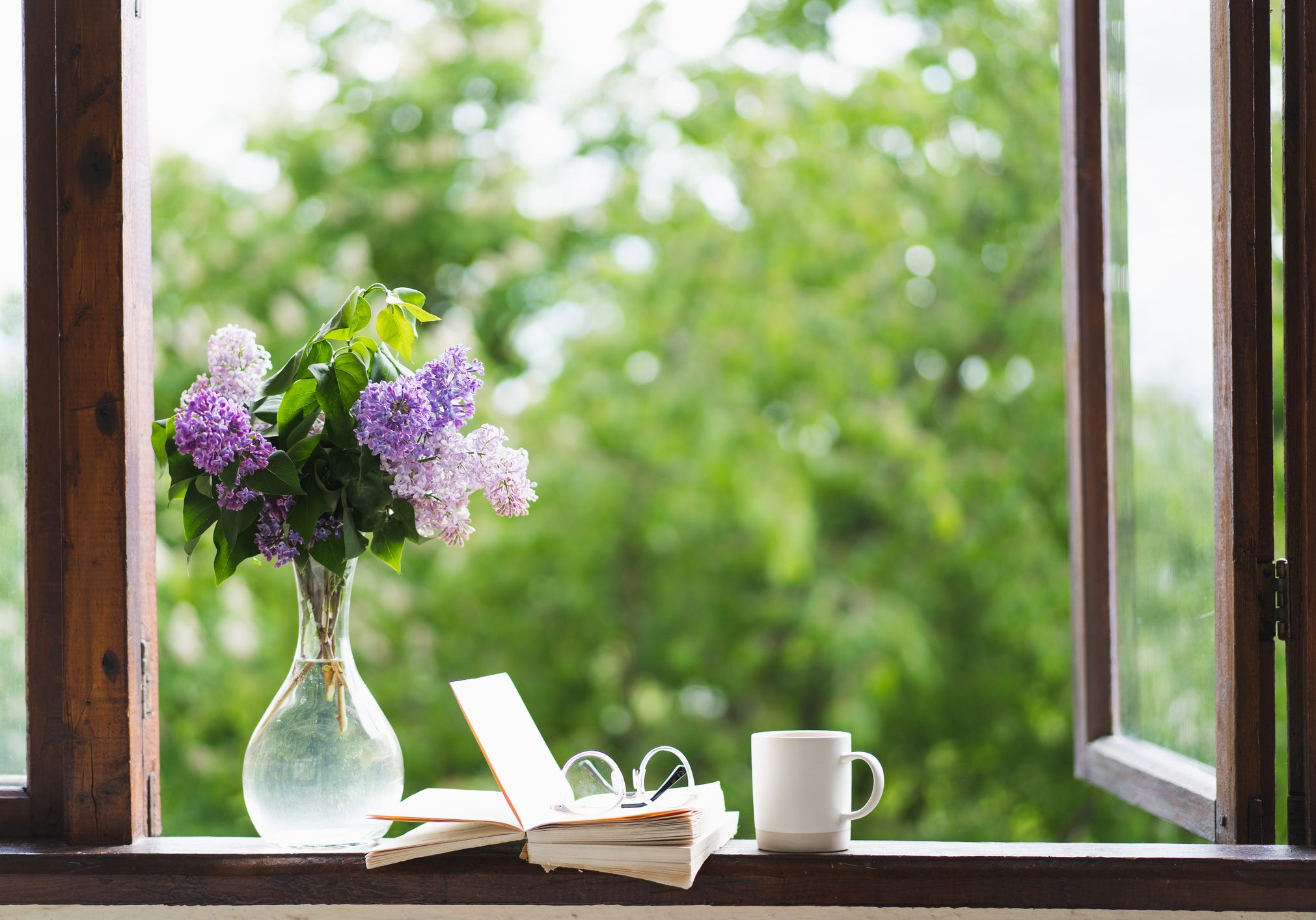 Book, glasses, cup of tea and lilac on a wooden window. Book, glasses, cup of tea and lilac on a wooden window. Fragrant tea in the garden. Romantic concept. Vintage style